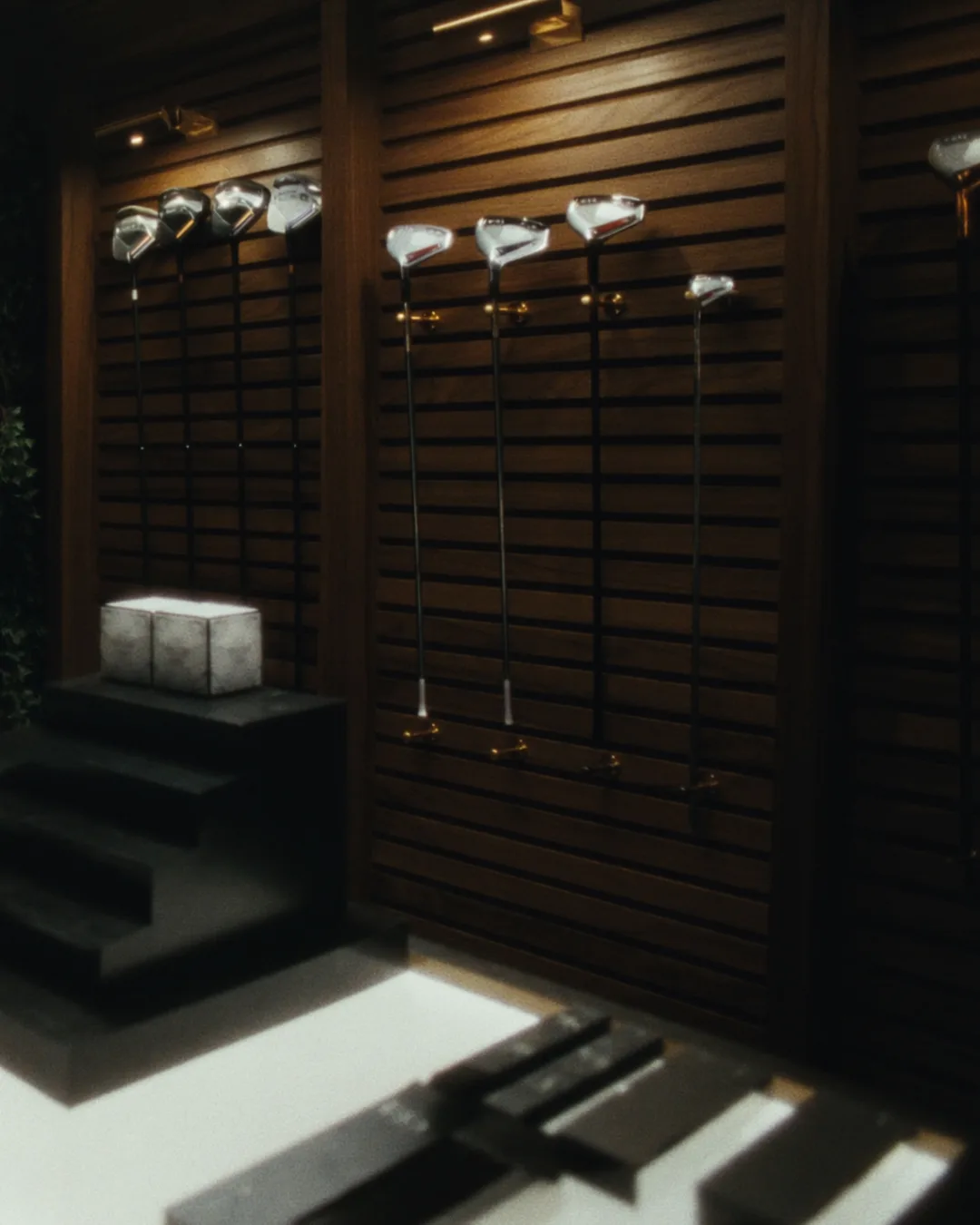 Walnut slat display wall in the Scratch pro shop with drivers and irons hung on gold pegs above a backlit counter